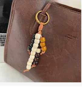Detail of colorful wooden beaded bag charm with gold clasp on brown leather tote