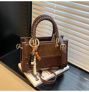 Détail d'un cabas en cuir marron avec poignée tressée et breloque en bois