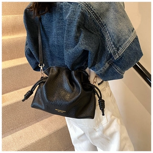 Detail of black drawstring bucket bag with litchi texture and gold hardware on a model