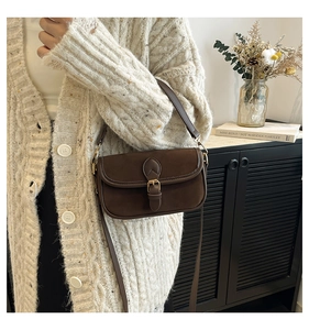 Detail of dark brown faux suede saddle bag with vintage buckle and gold hardware strap