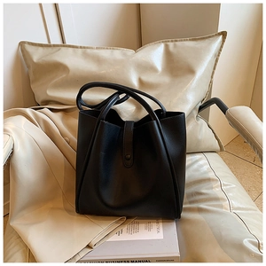 Détail d'un sac cabas en cuir noir avec anses renforcées sur un fauteuil élégant