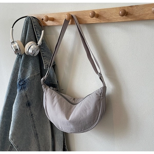 Detail view of a gray crescent nylon shoulder bag hanging on a wooden hook