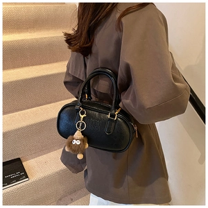 Détail du sac Boston en cuir noir avec logo embossé et breloque monstre en peluche
