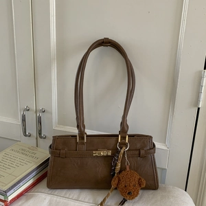 Close-up of brown retro shoulder bag with golden clasp and cute plush bear charm