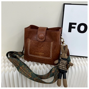 Brown PU leather bucket bag detail with colorful strap and plush rabbit charm
