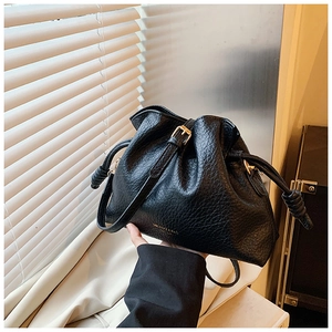 Detailed macro view of black lychee grain leather bucket bag with gold drawstring and knots