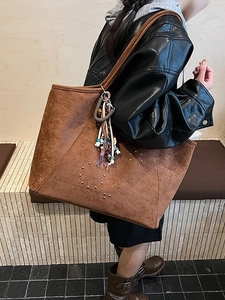Sac cabas en daim marron avec rivets et pompon bohème porté à l'épaule par un mannequin