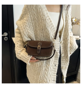 Close-up of a dark brown suede crossbody bag with gold metal buckle and thin shoulder strap