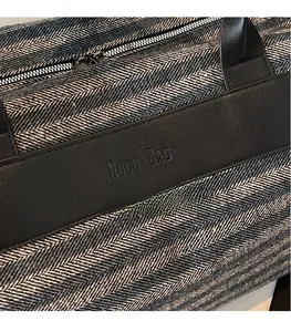 Close-up of herringbone fabric and black leather handles with embossed Noco BAG logo