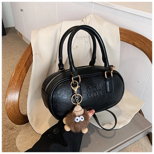 Détail du sac Boston en cuir grainé noir avec logo ATN et breloque monstre en peluche marron