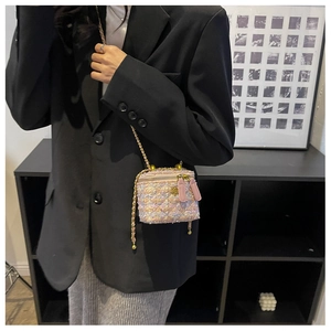 Détail d'un mini sac boîte en tweed rose avec chaîne dorée porté sur un blazer noir
