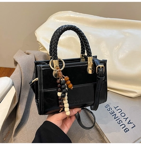 Détail du sac à bandoulière noir mat avec poignée tressée et pendentif en perles de bois