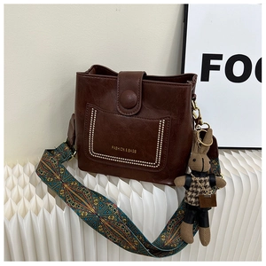 Close-up of brown leather bucket bag with ethnic strap and cute rabbit pendant