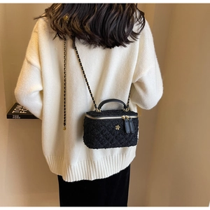 Close-up of black tweed vanity bag with gold flower buckle and chain shoulder strap