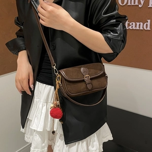 Detail of dark brown suede shoulder bag with metal buckle and red plush ball charm