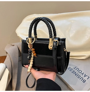 Détail d'un sac noir avec poignée tressée, perles en bois et finitions en métal doré chic