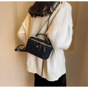 Close-up of black tweed box bag with gold floral clasp and woven chain strap detail