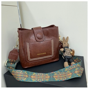 Detail of dark brown leather bucket bag with white stitching and colorful geometric strap