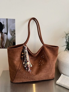 Sac cabas en daim marron avec rivets dorés et breloque bohème sur un bureau