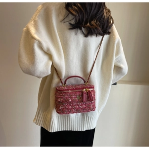Detail of pink tweed vanity bag featuring a golden flower emblem and chain strap