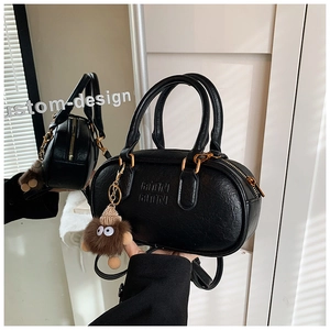 Close-up of litchi texture black mini Boston bag with golden zipper and plush monster charm
