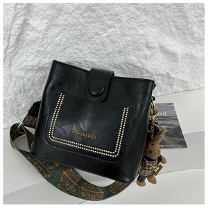 Detail of black leather bucket bag with printed strap and cute bunny doll accessory