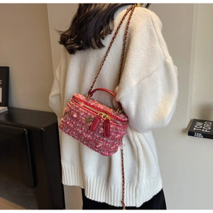 Detail of pink tweed box bag with red leather trim and golden flower logo on crossbody strap