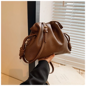 Macro view of brown lychee-pattern leather texture on a trendy drawstring bucket handbag