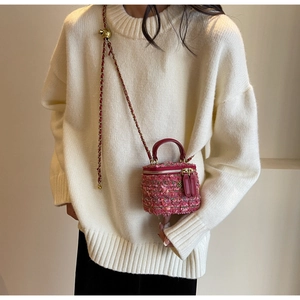 Pink tweed crossbody bag with chain strap and gold handle shown on a white sweater