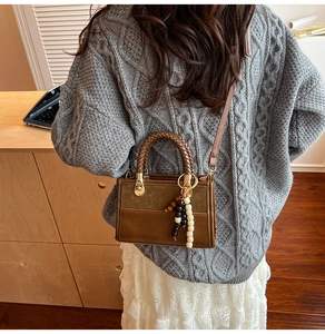 Détail d'un sac à main marron avec poignée tressée et charm en perles de bois naturel