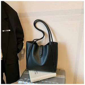 Détail du sac cabas en cuir noir avec fermeture à boucle posé sur une valise chic