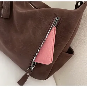 Detail view of the side zipper pocket on a brown tote bag holding a pink wallet