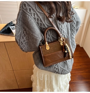 Détail d'un sac bandoulière marron avec poignée tressée et pompon en perles de bois chic