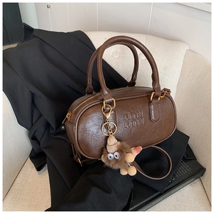Détail du sac Boston en cuir marron avec logo ATN gaufré et breloque en peluche monstre