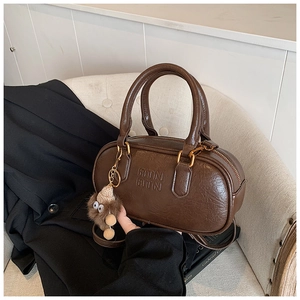 Detail of a brown glossy leather bowling bag with RTN embossed logo and plush charm