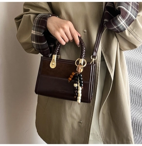 Détail du sac bandoulière avec poignée tressée, coutures en cuir mat et pendentif perlé