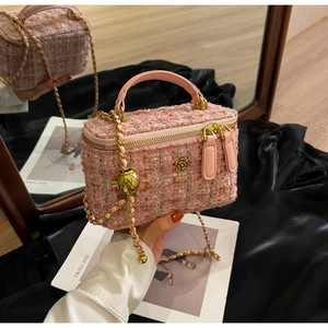 Detail of pink tweed box bag with gold camellia logo, chain strap, and zipper closure