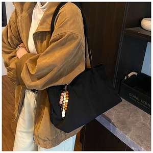 Détail d'un grand sac fourre-tout en toile noire avec pendentif en perles et plis latéraux