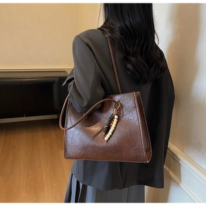 Detailed close-up of brown vintage leather tote bag with elegant beaded charm accessory