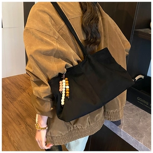 Gros plan d'un sac cabas noir en toile avec pendentif en perles sur l'épaule du mannequin