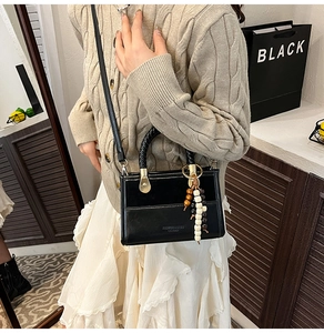 Petit sac noir avec pendentif perlé porté par un mannequin dans un cadre intérieur chic