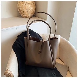 Grand sac cabas marron en cuir avec doubles poignées posé sur un canapé crème chic