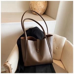 Détail du grand sac cabas en cuir mat marron foncé sur un fauteuil avec un blazer noir