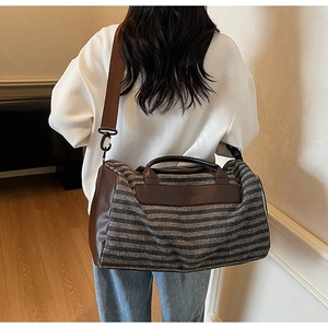 Detail of striped travel bag with brown leather handles worn by a model in home setting