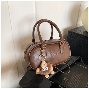 Detail of dark brown cylindrical crossbody bag with ATN embossed letters and plush charm