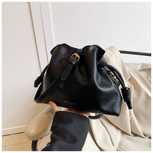 Macro detail of black drawstring bucket bag showing textured leather and gold lettering