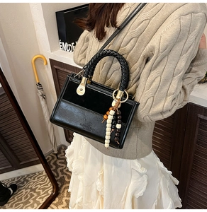 Détail d'un sac à bandoulière en cuir noir avec poignée perlée et logo mode gaufré