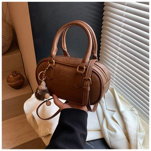 Close-up of brown retro Boston bag with ATN logo and plush charm detail on handle