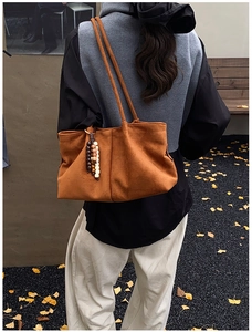 Détail d'un sac cabas en daim marron avec pendentif perlé porté à l'épaule par un mannequin