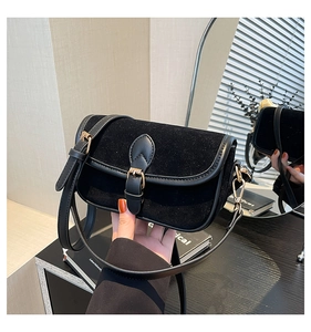 Detailed view of black suede shoulder bag with gold metal buckle and leather trim strap